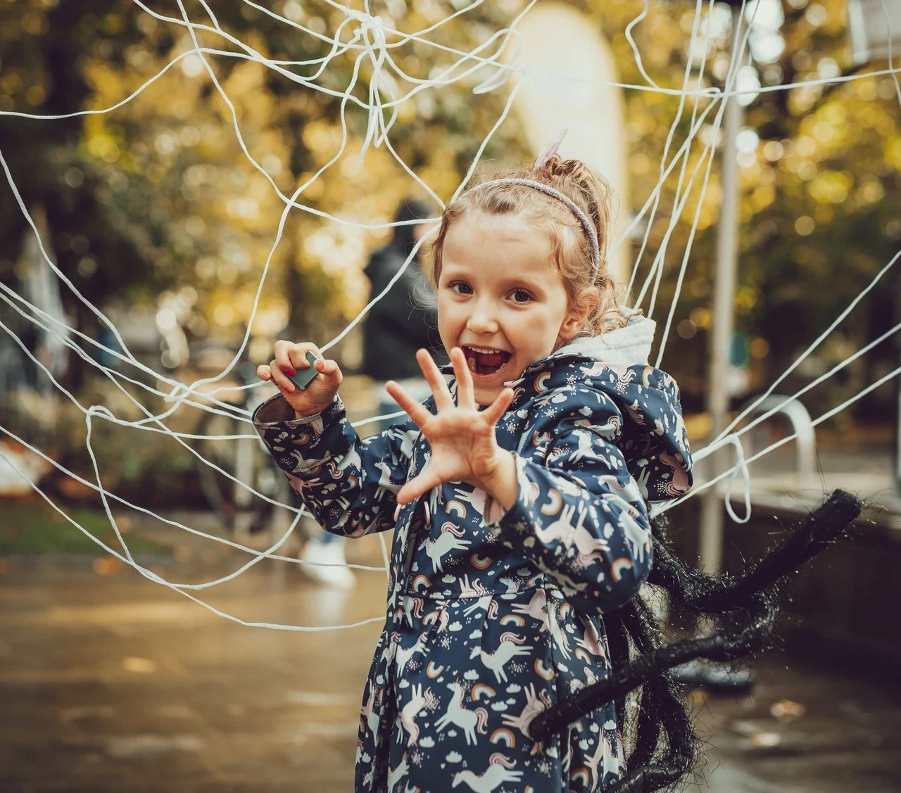 A girl, wearing a spider costume is doing a playful scary pose in front of a big cobweb made of string