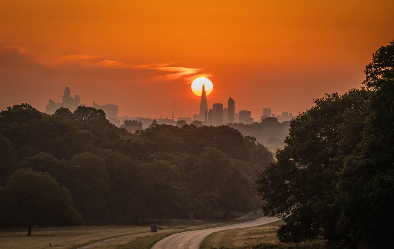 View of the sun setting behind the skyscrapers of London, against a deep orange sky.