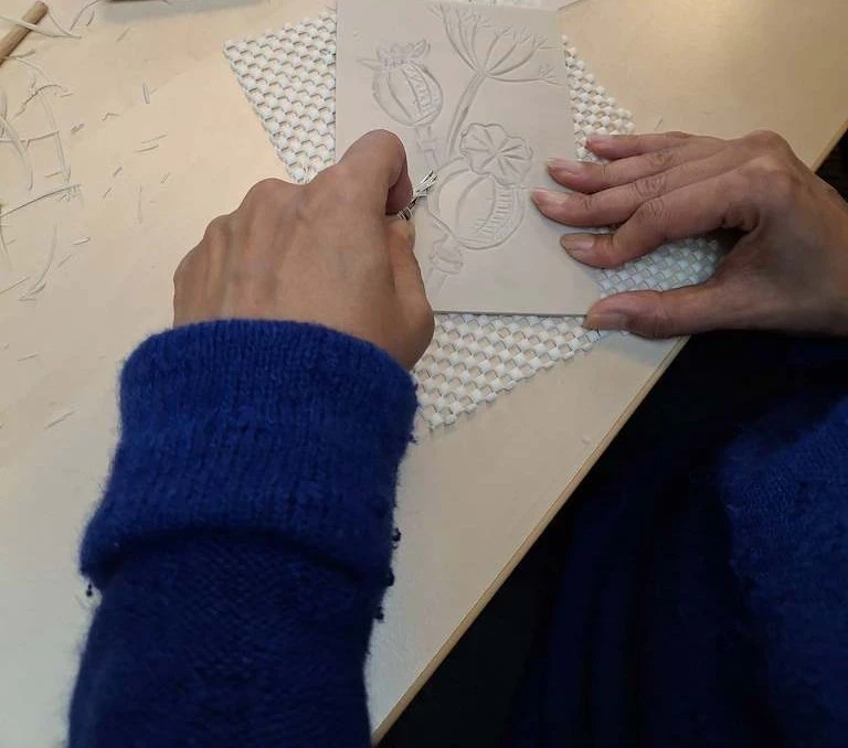 Close up of two hands carving a seed head on lino