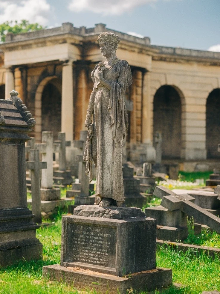 Image of a statue on a gravestone with a cemetery backdrop