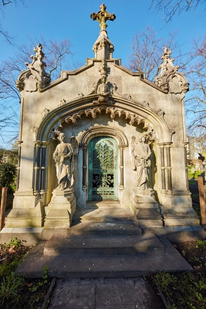 Grand mausoleum place above a crypt, made of white stone with 3 stairs leading up to it.